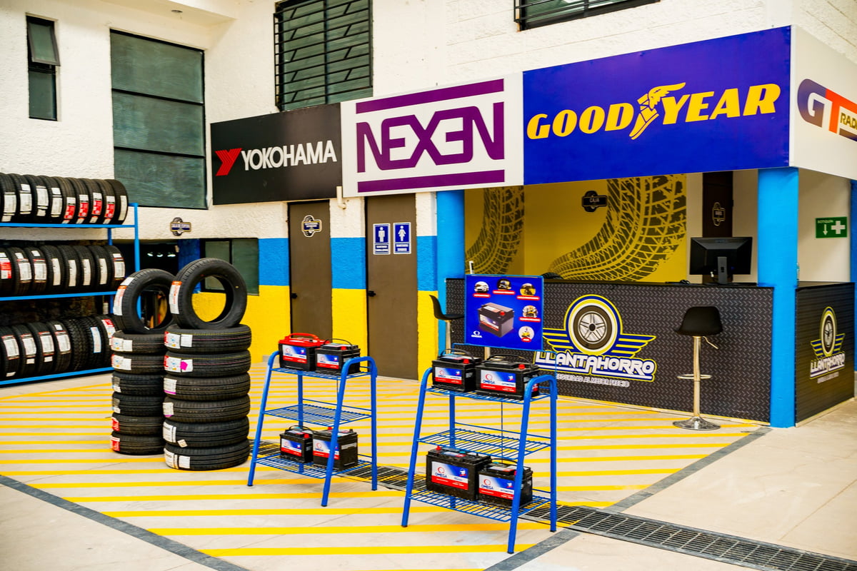 Tire shop showroom with Goodyear and Nexen brand displays, shelved tires, and blue service stands on yellow striped floor