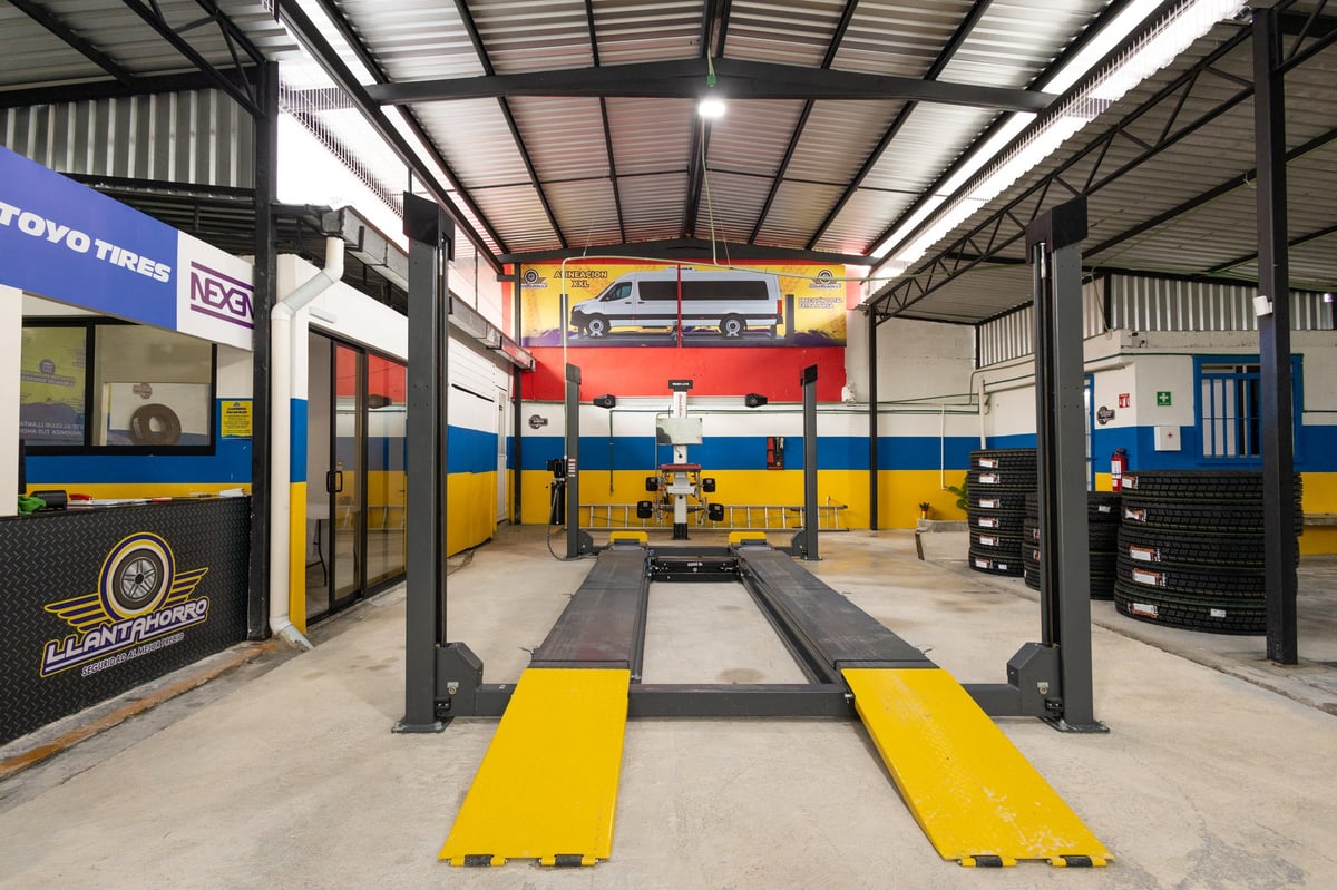 Professional car repair garage with yellow lift platform and red vehicle suspended on hydraulic lift in the bay