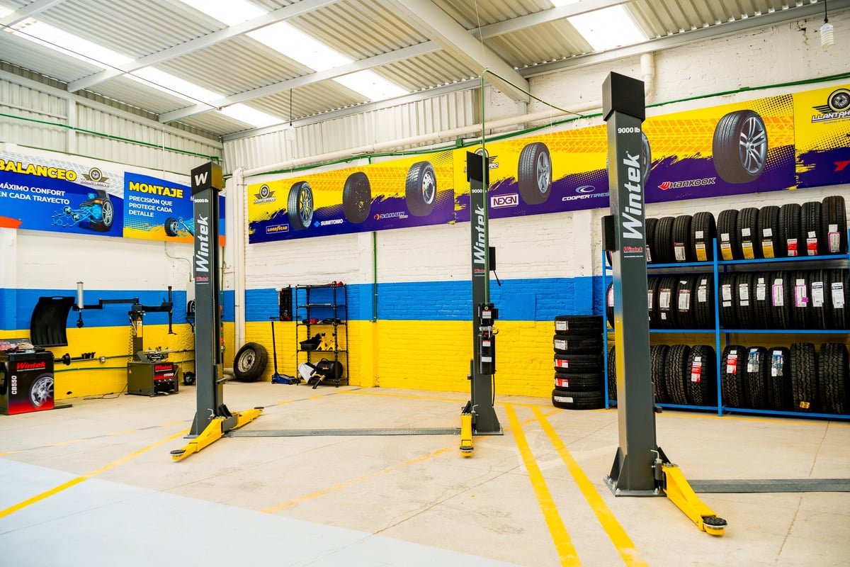 Professional car service garage with two yellow and black hydraulic lifting ramps, tools storage, and a large car service advertisement on the wall