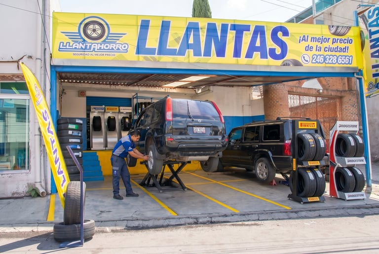 Tire shop storefront with blue and yellow signage displaying LLANTAS, showing a vehicle being serviced inside the garage