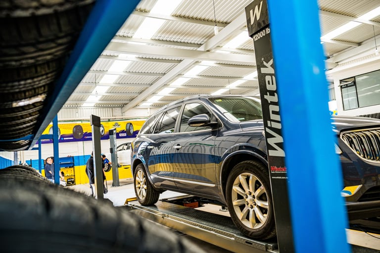 Dark sedan on a vehicle transport trailer at an auto auction or transport facility with blue steel frame and industrial ceiling