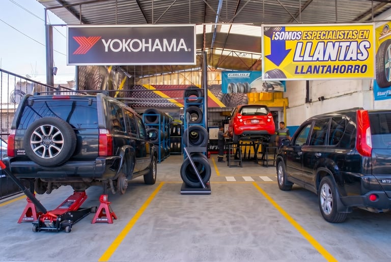 Auto repair and tire shop interior with multiple vehicles on hydraulic lifts and tire equipment visible under industrial warehouse ceiling
